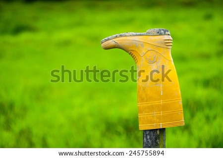 Damage and dirty yellow wellington  boots on wood pole with green grass background image suitable for background purpose