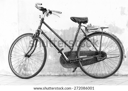 Retro styled black and white image of old bicycle isolated on a white wall background.