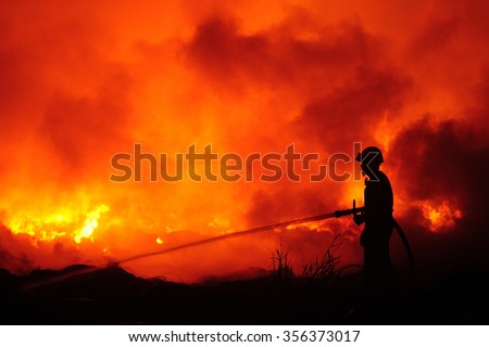 Silhouette of fireman fighting bushfire at night.