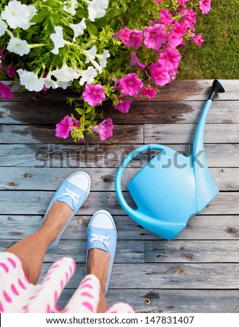 Woman with watering can and flowers on a patio deck