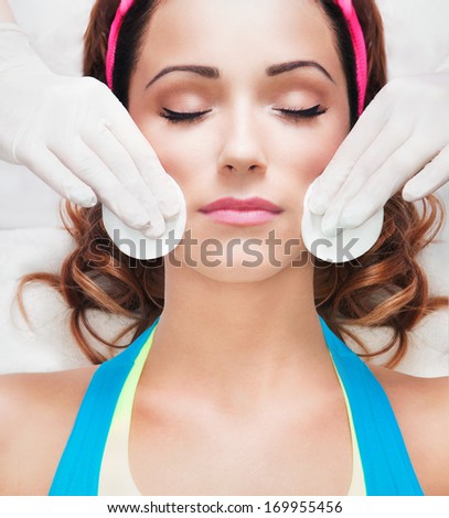 Woman getting face treatment in medical spa center, cleansing with cosmetic cotton pads