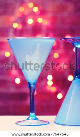 Two turquoise martini glasses, brick wall and fairy lights in the background, funky colors