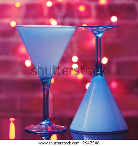 Two turquoise martini glasses, brick wall and fairy lights in the background, funky colors