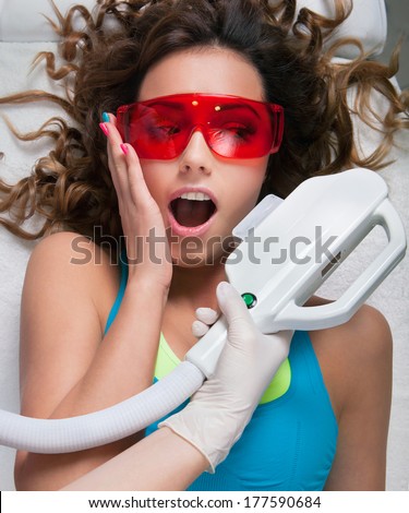 Woman getting laser face treatment in medical spa center, funny expression, hesitation, pain concept
