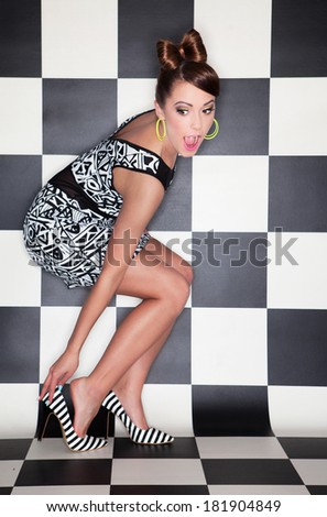 Attractive surprised young woman wearing high heels on checkered background,  fashion concept