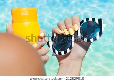 Summer fashion and beauty hand care concept, woman holding sunglasses and sunscreen lotion at the pool