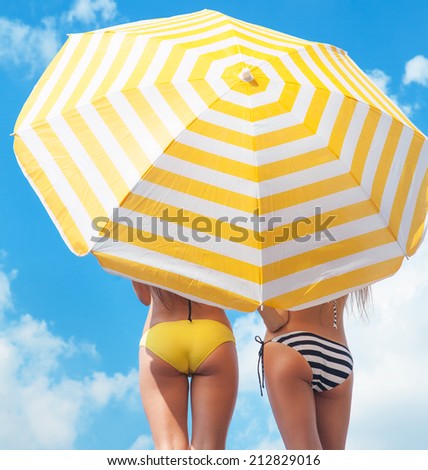 Sun protection and summer body care concept, women wearing bikini under a beach umbrella