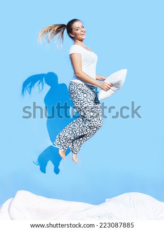 Happy morning concept, woman holding a pillow jumping up on bed