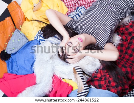 Nothing to wear concept, young attractive woman lying down on a pile of clothes