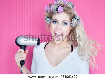 Young attractive happy laughing blonde woman with hair dryer and rollers