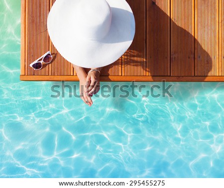Summer holiday fashion concept - tanning woman wearing sun hat on a wooden pier view from above