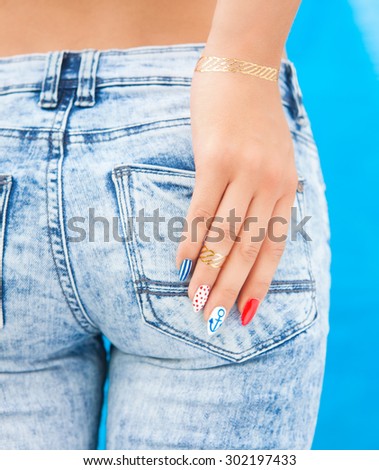 Young woman with marine sailor gel nails manicure holding hand at jeans back pocket