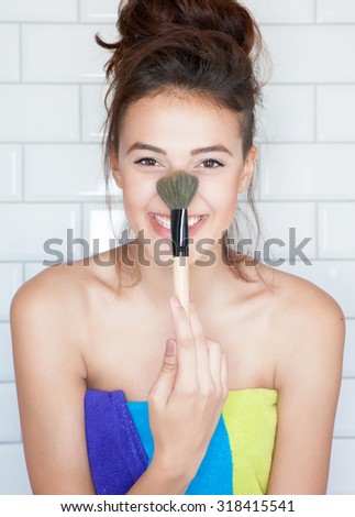 Applying make up concept, young attractive smiling woman covered with towel with cosmetic brush