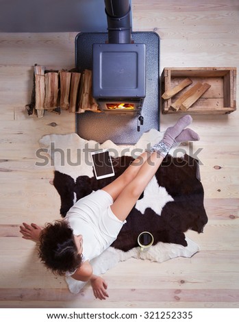 Young woman with cup of coffee sitting home on a cow rug by the fireplace. Fall winter relaxing and leisure concept.