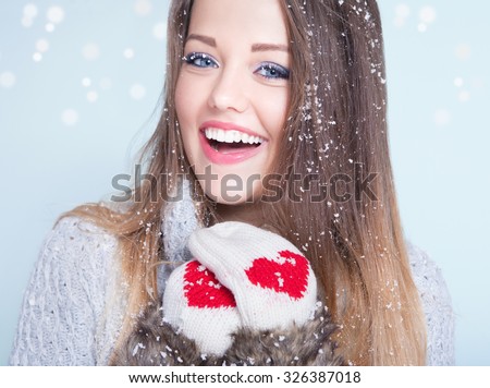 Beautiful happy smiling young woman wearing winter gloves covered with snow flakes. Christmas portrait concept.