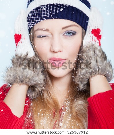 Beautiful happy winking young woman wearing winter hat and gloves covered with snow flakes. Christmas portrait concept.
