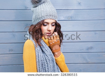 Beautiful natural young brunette woman with eyes closed wearing knitted sweater, leather gloves, scarf and hat. Hair covered with snow flakes. Fall and winter fashion concept.