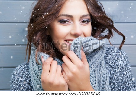 Beautiful natural looking young smiling brunette woman, wearing knitted scarf, covered with snow flakes. Snowing winter beauty concept.