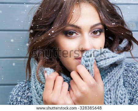 Beautiful natural looking young smiling brunette woman, wearing knitted scarf, covered with snow flakes. Snowing winter beauty concept