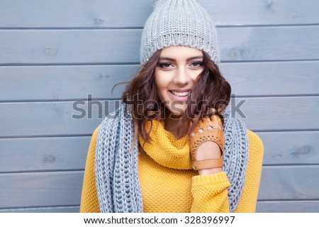 Beautiful natural young smiling brunette woman wearing knitted sweater, leather gloves, scarf and hat. Covered with snow flakes. Fall and winter fashion concept.