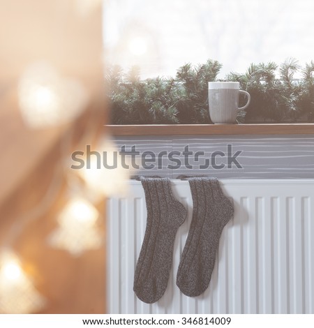 Winter woolen socks drying on a heater, christmas lights, decorations and hot drink