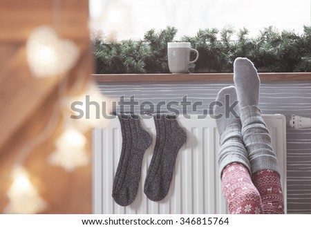 Woman warming up with feet on heater Winter woolen socks drying on a heater, christmas lights, decorations and hot drink