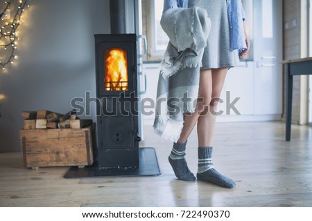 Young woman wearing winter socks standing home holding a blanket by the fireplace. Wooden cabin interior.