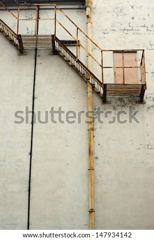 The rusty iron ladder is attached on an old brick wall