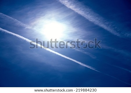 the bright white sun and traces from white exhausts of jet planes in the dark blue sky