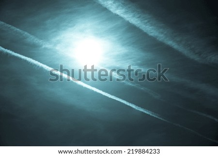 the bright white sun and traces from white exhausts of jet planes in the dark turquoise sky