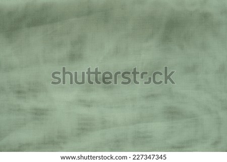 the textured background of green color with tone spots from synthetic fabric in a grid with small cells