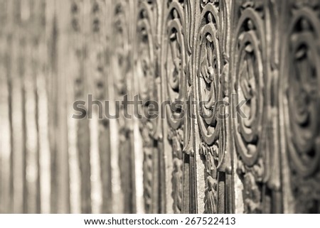 fragment of an ancient pig-iron fence with the abstract forged pattern of beige color