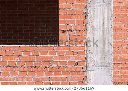 brick wall under construction with a window opening and concrete part of a column