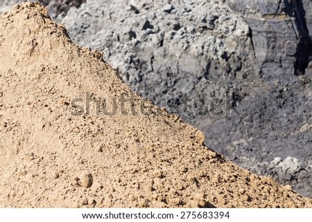 heap of yellow construction sand in the form of a pyramid on a gray background of soil