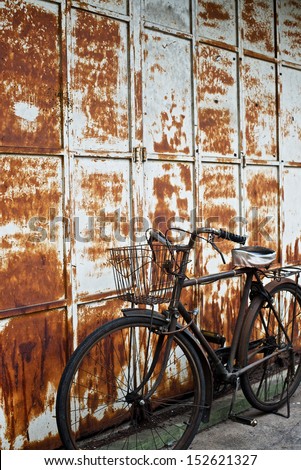 An old rusty bicycle parked next to an old metal sliding door with peeling paint work.