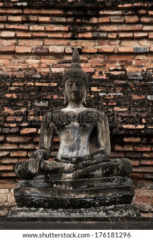 Old seasoned statue of Buddha on classic textured brick wall on portrait orientation.