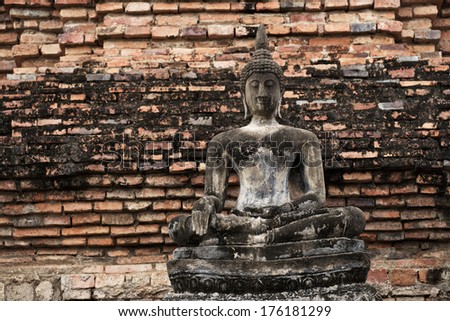 Old seasoned statue of Buddha on classic textured brick wall on landscape orientation.