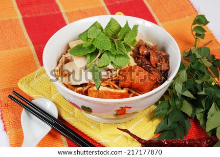 A bowl of Asian curry noodles on colourful table mat decorated with green curry leaves.