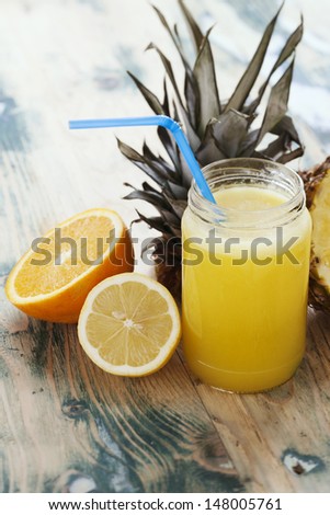 Fresh squeezed orange,lemon and pineapple juice arranged with fruits on wooden rustic table. Shot at daylight, shallow depth of field.