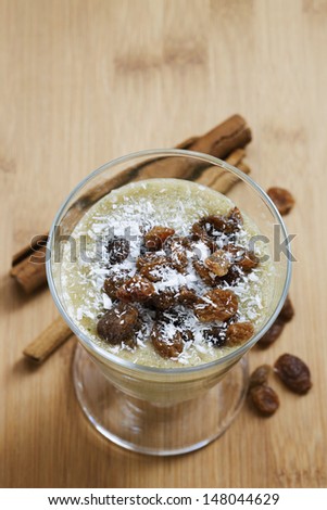 Healthy creamy smoothie with dried raisins and shredded coconut decoration on wooden table. Studio shot on daylight, shallow depth of field.