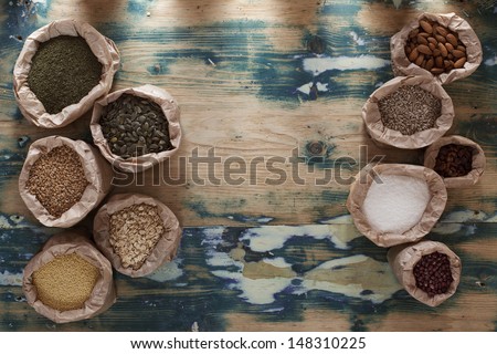 Healthy mix. Various types of beans, seeds, nuts and grains in paper bags on a rustic wooden table. Grain texture added.
