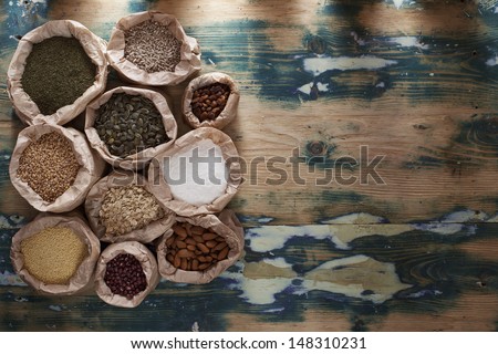 Healthy mix. Various types of beans, seeds, nuts and grains in paper bags on a rustic wooden table. Grain texture added.