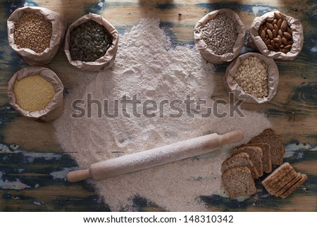 Grains and whole wheat flour. Various types of seeds, nuts, grains in paper bags and spilled flour with rolling pin on the rustic wooden table. Grain texture added.