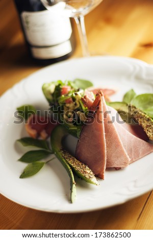 Prosciutto ham with vegetables on a plate and wine bottle in the background.