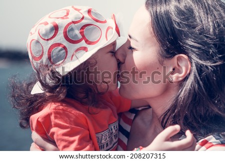 Sensual portrait of a beautiful mother and little daughter kissing outdoors