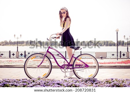 stylish girl hipster posing near cruiser bicycle near the flowerbed