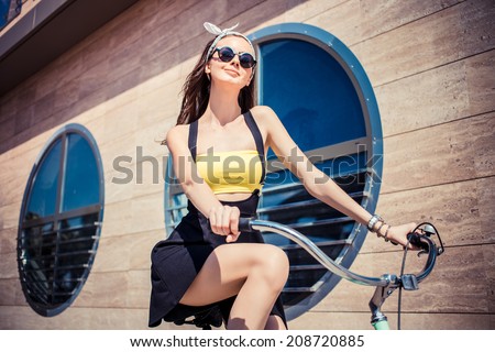 Portrait of a stylish girl hipster riding a  cruiser bicycle against the background of the building with round windows