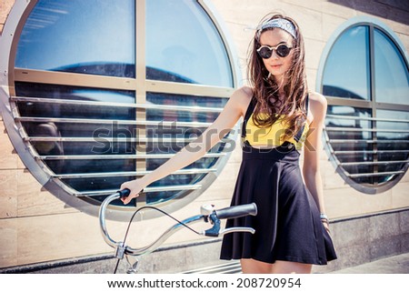 Portrait of a stylish girl hipster riding a  cruiser bicycle against the background of the building with round windows