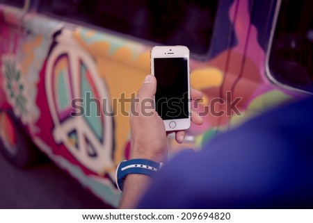 Hand holding white smartphone with black screen on retro car background
