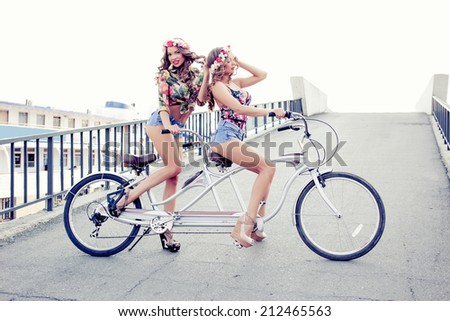 two beautiful girls twins ride on a tandem bike outdoors